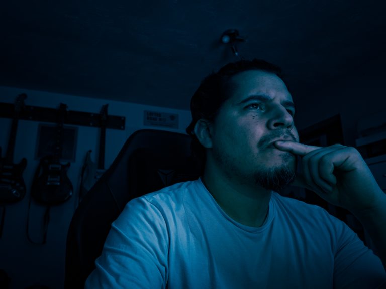 A writer sits alone at his desk in low blue light, gazing at the screen in quiet concentration.